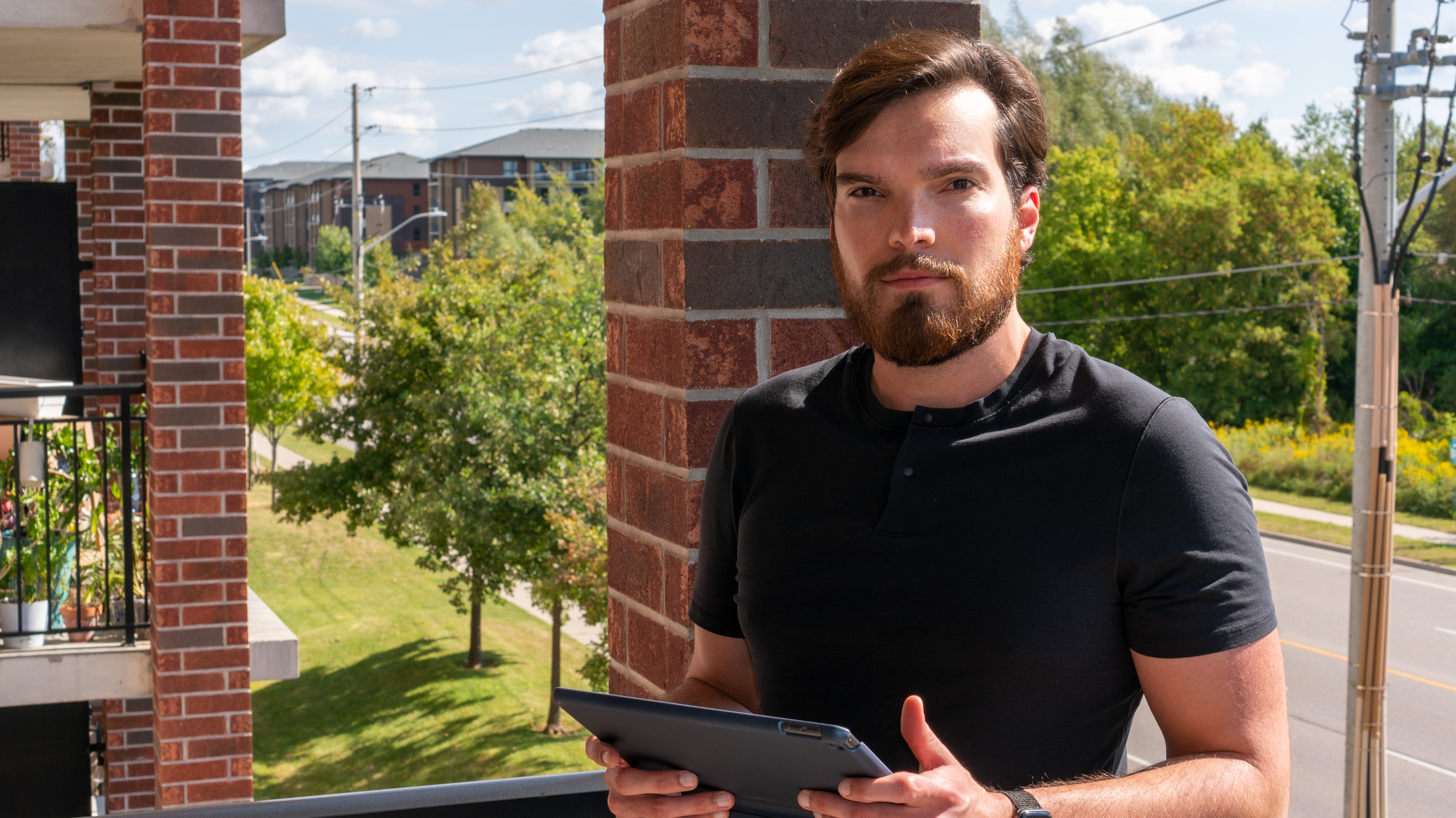 A picture of Brennan Chapman outdoors, in a black t-shirt, holding an iPad.